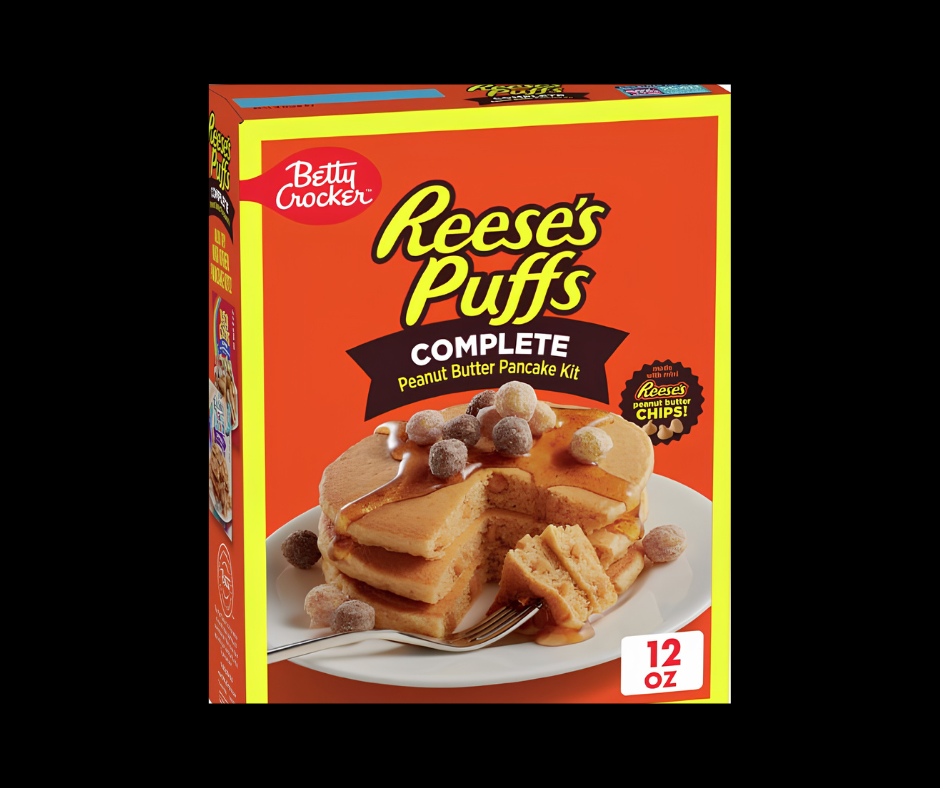 A box of Betty Crocker Reese's Puffs Complete Peanut Butter Pancake Kit, featuring a bright orange and yellow packaging design with an image of pancakes topped with Reese's Puffs and syrup.